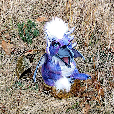 image of what appears to be a small stuffed dragon hatching from a gold shell at Robinhood Farm, slightley edited by Charlie Ipcar, Graphic © 2026, Ipbar Productions, all rights reserved.